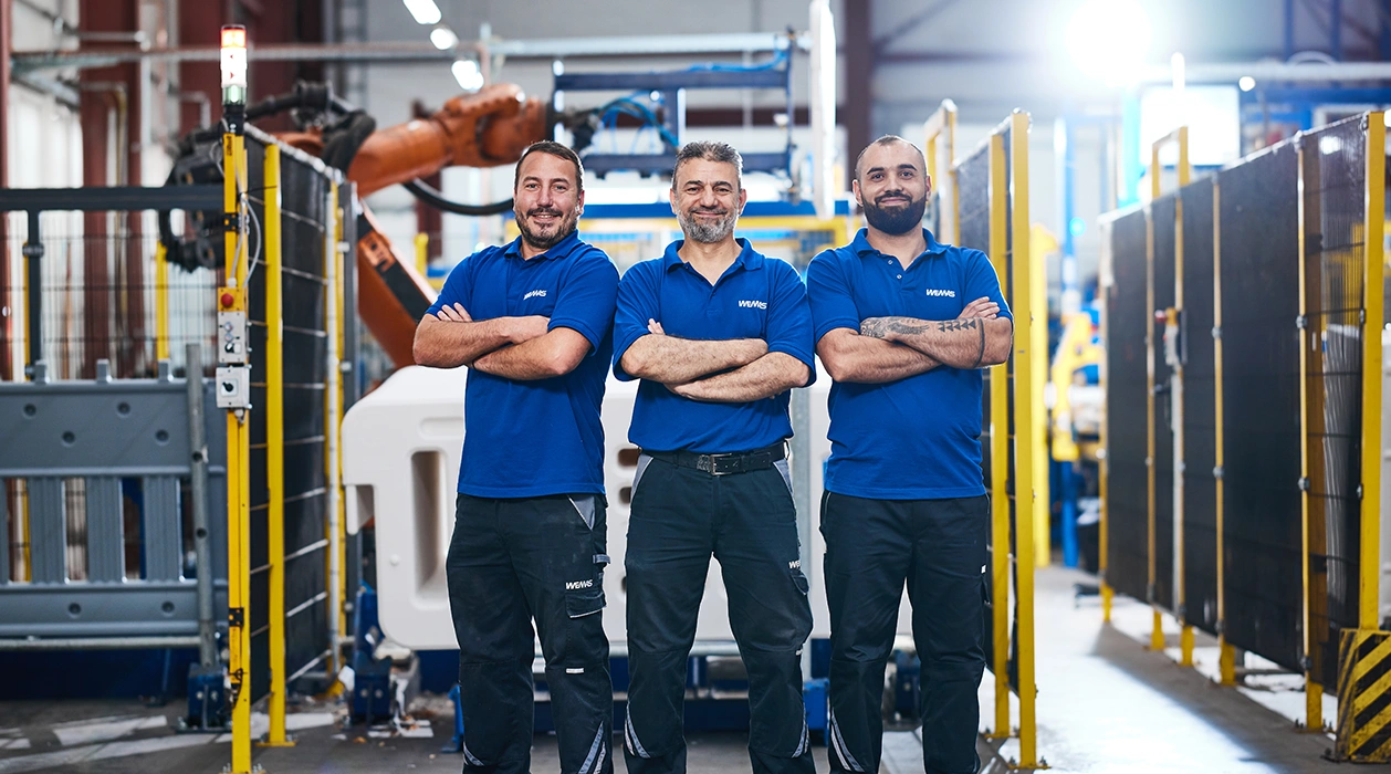 Drei Mitarbeiter von WEMAS stehen in der Produktion und schauen in die Kamera.